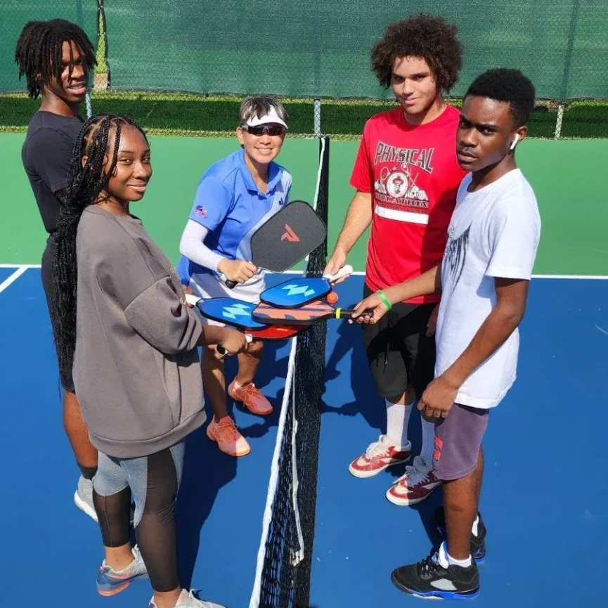 A group of people standing around a tennis court.